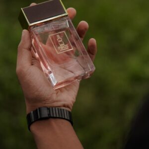 Close-up of a hand holding a luxury perfume bottle against a blurred green background, showcasing elegance.