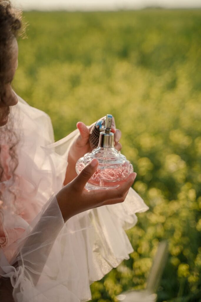 A woman in a dress holds a perfume bottle in a sunny, blooming field.
