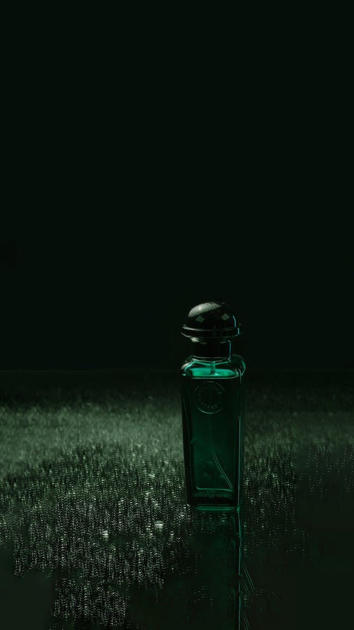 Close-up of a green perfume bottle on reflective surface, dark ambiance.